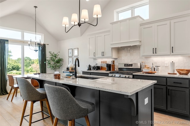 kitchen featuring gas stove, a kitchen island with sink, a notable chandelier, white cabinets, and decorative light fixtures