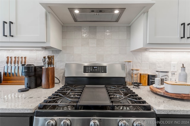 kitchen featuring gas stove, light stone counters, tasteful backsplash, ventilation hood, and white cabinetry