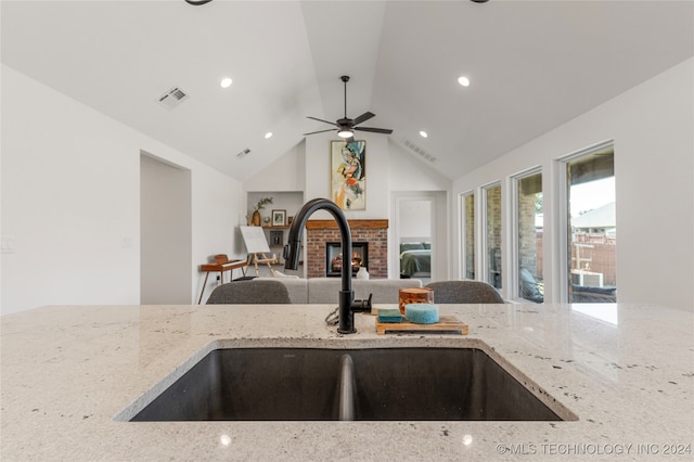 kitchen with ceiling fan, vaulted ceiling, light stone countertops, and sink