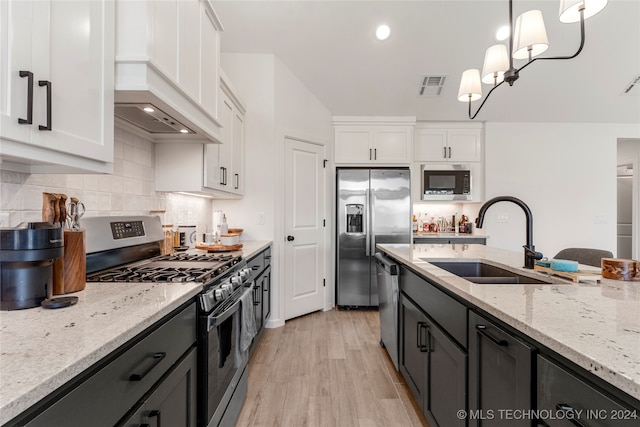 kitchen featuring light stone counters, sink, white cabinets, appliances with stainless steel finishes, and decorative light fixtures