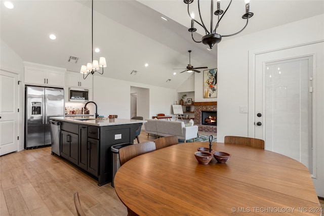 dining area with lofted ceiling, sink, a brick fireplace, light hardwood / wood-style flooring, and ceiling fan with notable chandelier