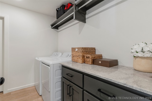 laundry area featuring light wood-type flooring, washer and dryer, and cabinets