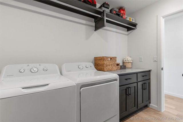 clothes washing area with washing machine and clothes dryer, light hardwood / wood-style floors, and cabinets