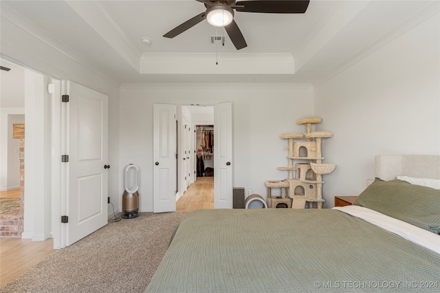 bedroom with ceiling fan, a tray ceiling, light carpet, and ornamental molding