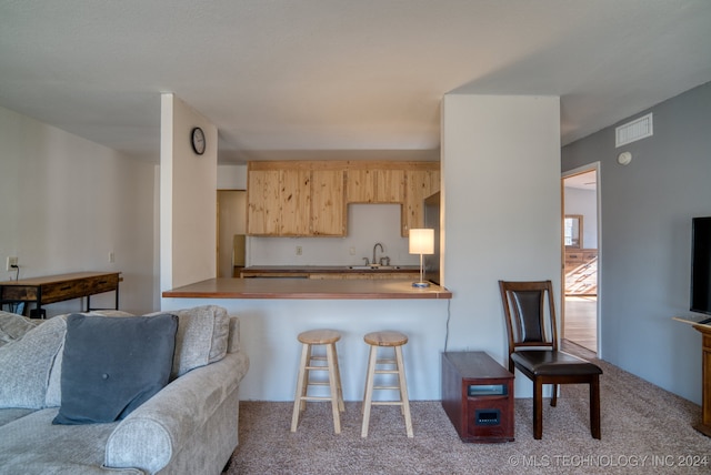 kitchen with a breakfast bar area, light carpet, kitchen peninsula, sink, and light brown cabinetry