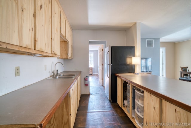 kitchen with light brown cabinetry, sink, and stainless steel fridge