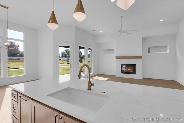 kitchen with light stone countertops, pendant lighting, light brown cabinetry, ceiling fan, and sink