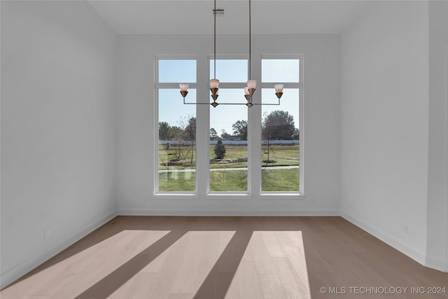 unfurnished dining area with hardwood / wood-style flooring, crown molding, and a chandelier