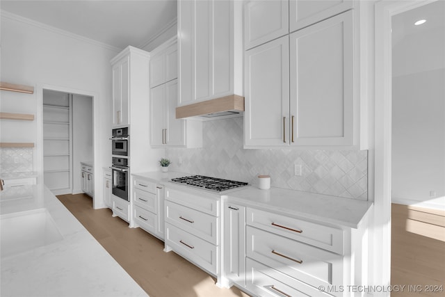 kitchen with white cabinets, tasteful backsplash, hardwood / wood-style flooring, light stone countertops, and crown molding