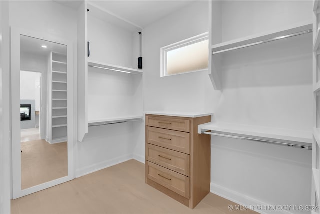 spacious closet with a multi sided fireplace and light hardwood / wood-style flooring