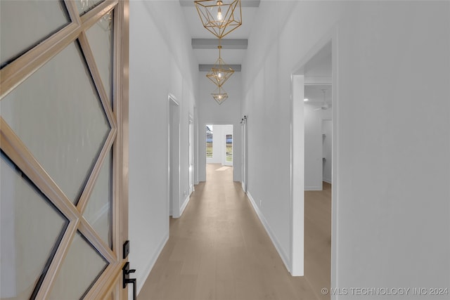 hallway with an inviting chandelier, light hardwood / wood-style flooring, and a towering ceiling