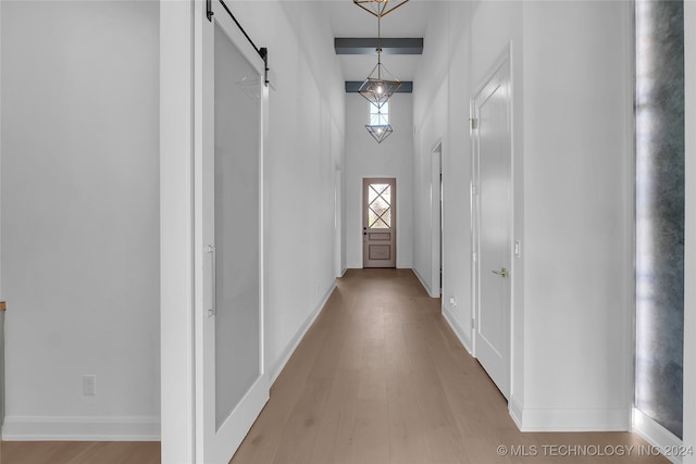 hallway featuring a towering ceiling, beam ceiling, light hardwood / wood-style floors, and a barn door