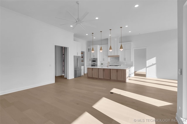 kitchen featuring a large island with sink, white cabinets, hanging light fixtures, light hardwood / wood-style flooring, and stainless steel appliances