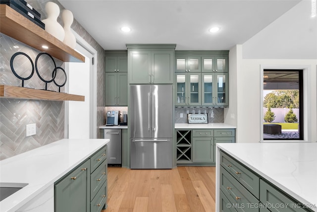 kitchen featuring stainless steel refrigerator, backsplash, green cabinetry, and light hardwood / wood-style flooring