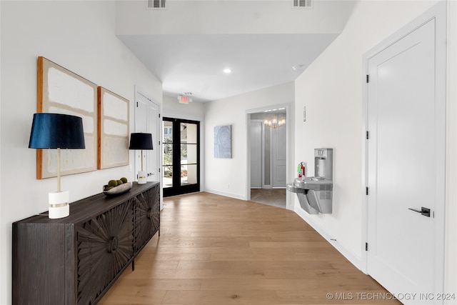 interior space featuring light wood-type flooring, an inviting chandelier, and french doors