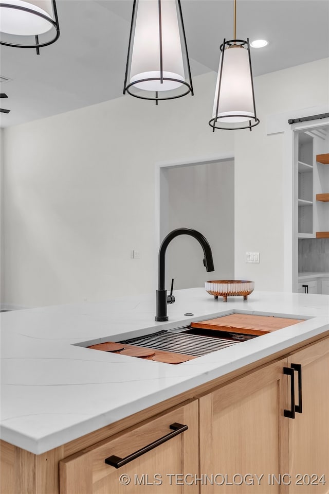 kitchen with light stone countertops, light brown cabinets, and hanging light fixtures