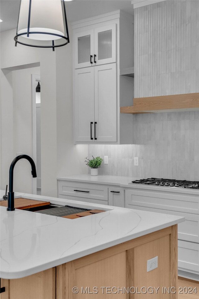 kitchen featuring light stone counters, white cabinets, hanging light fixtures, tasteful backsplash, and gas stovetop