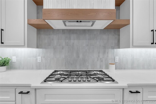 kitchen with light stone counters, backsplash, stainless steel gas stovetop, and white cabinetry