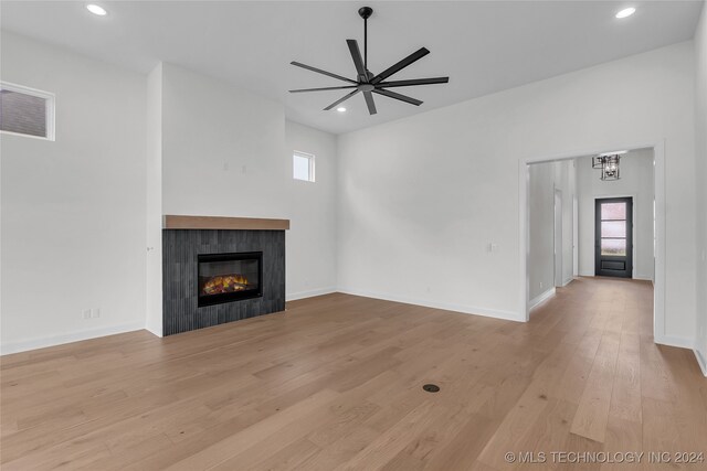 unfurnished living room with ceiling fan with notable chandelier, a tiled fireplace, light hardwood / wood-style floors, and plenty of natural light