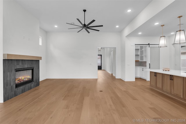 unfurnished living room featuring a barn door, a tiled fireplace, ceiling fan, and light hardwood / wood-style flooring