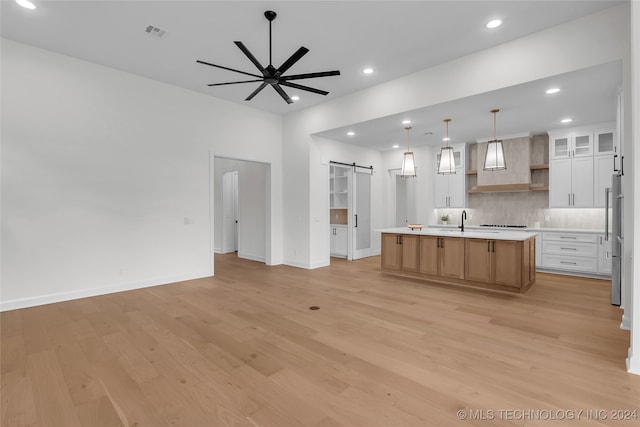 kitchen featuring ceiling fan, white cabinets, a center island with sink, a barn door, and light hardwood / wood-style floors