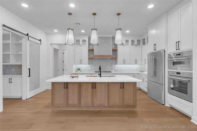 kitchen featuring white cabinets, a center island with sink, stainless steel appliances, and a barn door