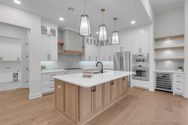 kitchen with light wood-type flooring, a kitchen island with sink, beverage cooler, and white cabinetry