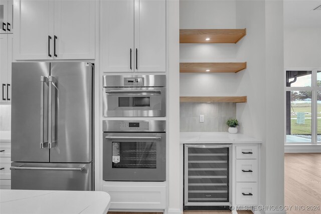 kitchen featuring beverage cooler, white cabinets, light hardwood / wood-style floors, and stainless steel appliances