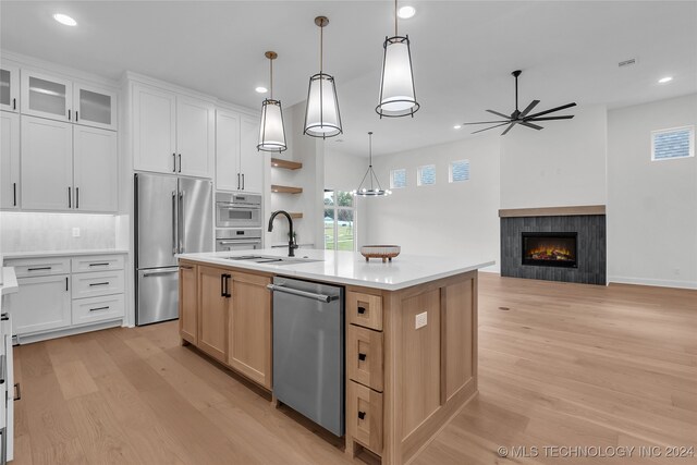 kitchen featuring white cabinetry, appliances with stainless steel finishes, a tile fireplace, and a kitchen island with sink