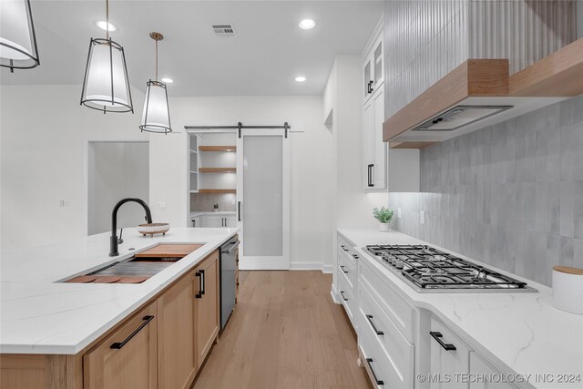 kitchen with pendant lighting, white cabinetry, sink, and a barn door