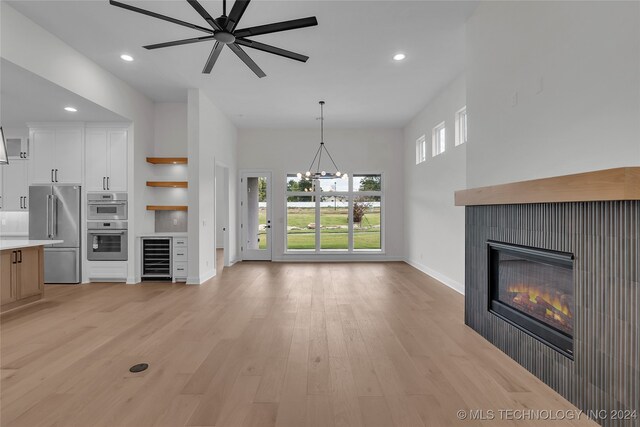 unfurnished living room with light wood-type flooring, ceiling fan with notable chandelier, and wine cooler