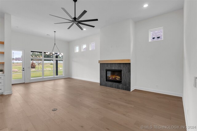 unfurnished living room with ceiling fan with notable chandelier, a tiled fireplace, and light hardwood / wood-style flooring