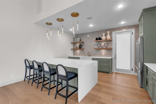 kitchen with sink, kitchen peninsula, high end fridge, light hardwood / wood-style flooring, and a breakfast bar