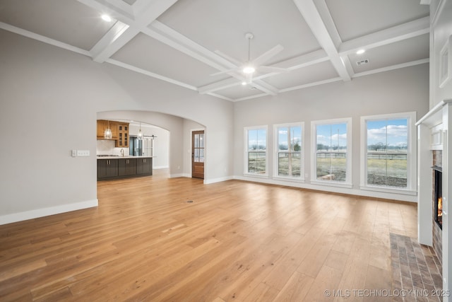 unfurnished living room featuring a towering ceiling, beamed ceiling, a chandelier, coffered ceiling, and light hardwood / wood-style floors