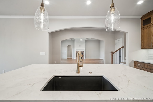 kitchen with light stone counters, hanging light fixtures, ornamental molding, and sink