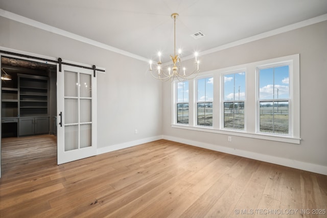 unfurnished dining area featuring an inviting chandelier, crown molding, wood-type flooring, and a barn door