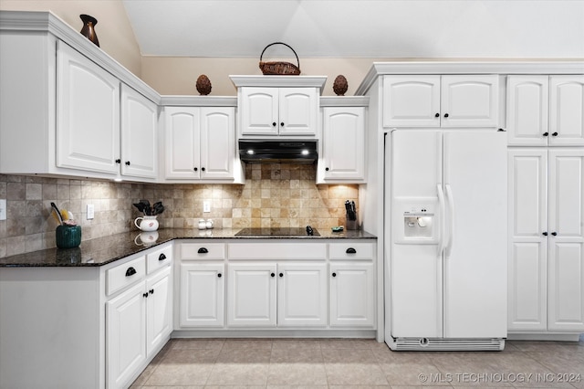 kitchen featuring white refrigerator with ice dispenser, dark stone counters, backsplash, and white cabinetry