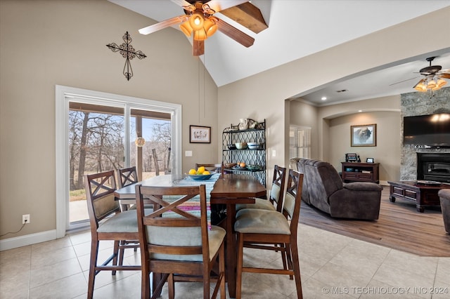 dining space with light tile patterned floors, a large fireplace, ceiling fan, and high vaulted ceiling