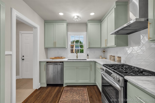 kitchen featuring appliances with stainless steel finishes, dark hardwood / wood-style flooring, wall chimney range hood, sink, and green cabinets