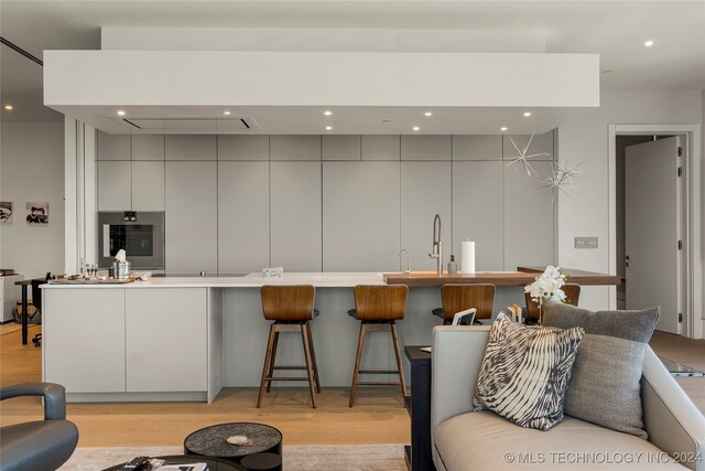 kitchen featuring white cabinets, sink, light hardwood / wood-style flooring, oven, and a kitchen breakfast bar