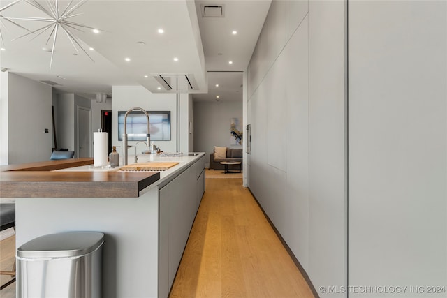 kitchen with white cabinets, a spacious island, light wood-type flooring, and sink