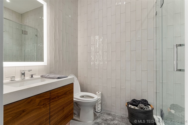 bathroom featuring vanity, tile walls, toilet, and a shower with door