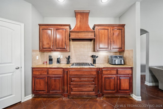 kitchen with premium range hood, dark tile patterned flooring, tasteful backsplash, stainless steel gas stovetop, and light stone countertops