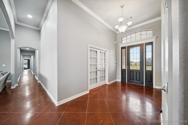 tiled entrance foyer with a chandelier, ornamental molding, and high vaulted ceiling