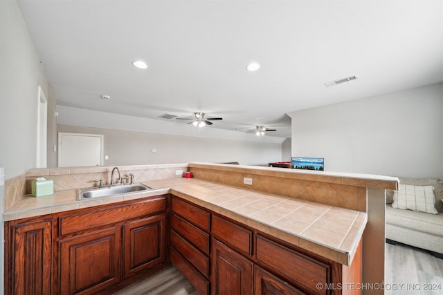 kitchen with light wood-type flooring, sink, kitchen peninsula, tile countertops, and ceiling fan