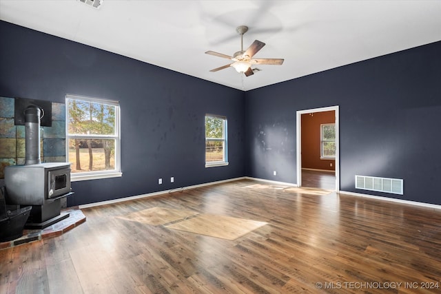 unfurnished room featuring a wood stove, ceiling fan, wood-type flooring, and a healthy amount of sunlight