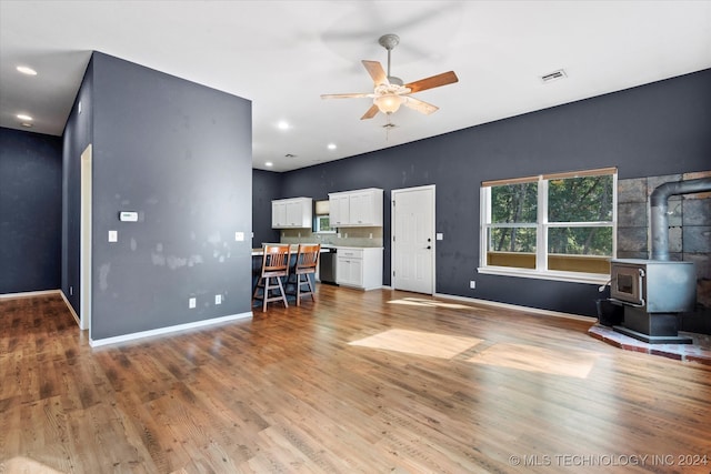 unfurnished living room featuring light hardwood / wood-style floors, ceiling fan, and a wood stove