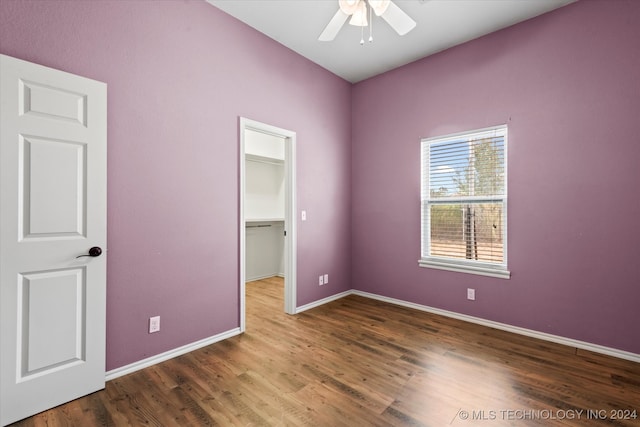 unfurnished bedroom featuring ceiling fan, a closet, hardwood / wood-style floors, and a walk in closet