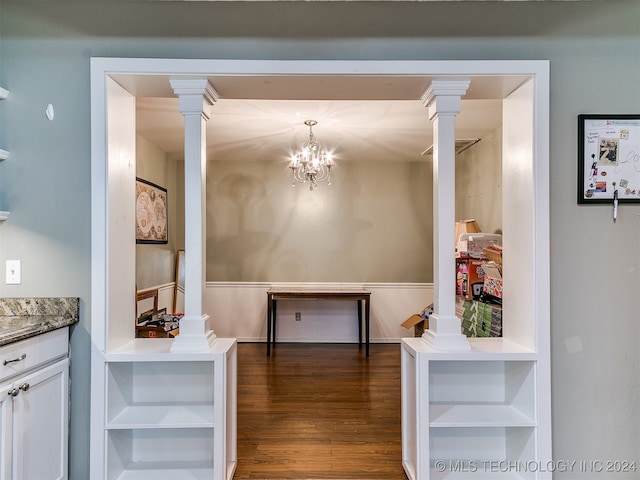 interior space featuring ornate columns, a notable chandelier, dark wood-type flooring, and built in shelves