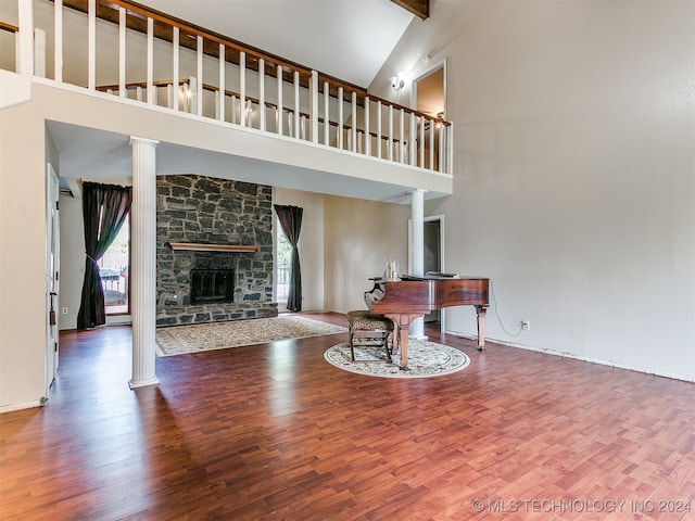 living room with hardwood / wood-style flooring, beam ceiling, high vaulted ceiling, a stone fireplace, and ornate columns